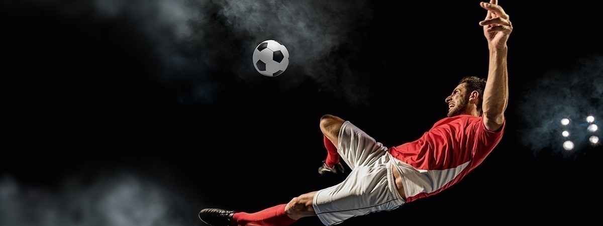 Football player in red and white uniform hitting ball from mid-air position.