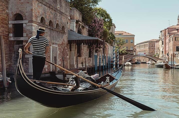 Gondoliere steering a gondola through one of the multiple Venetian canals.