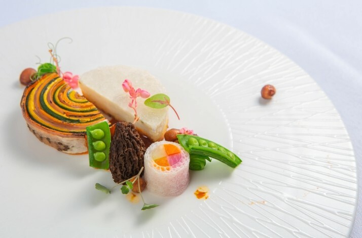 A white plate with a decorated dish, featuring a colorful slices of vegetables and green peas.