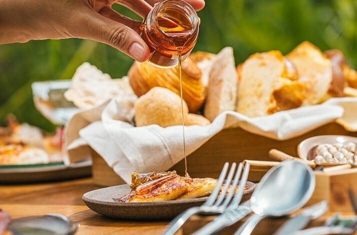 Close-up of a hand pouring honey made by native stingless bees from the Serra da Mantiqueira region over toast at NOTIÊ Restaurante.