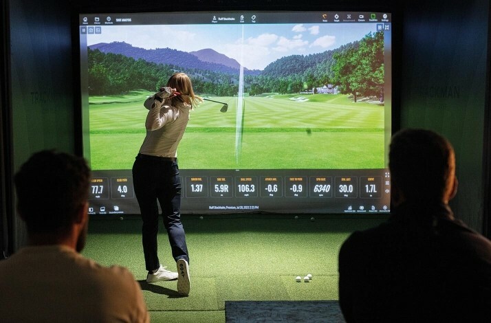 A golfer taking a swing on a state-of-the-art simulator photographed from the back.