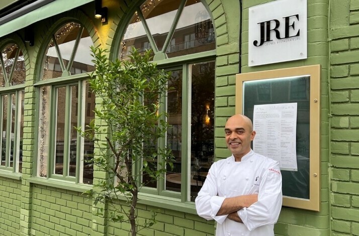 Chef Alfred Prasad standing next to the JRE sign on the facade on restaurant Shiuli