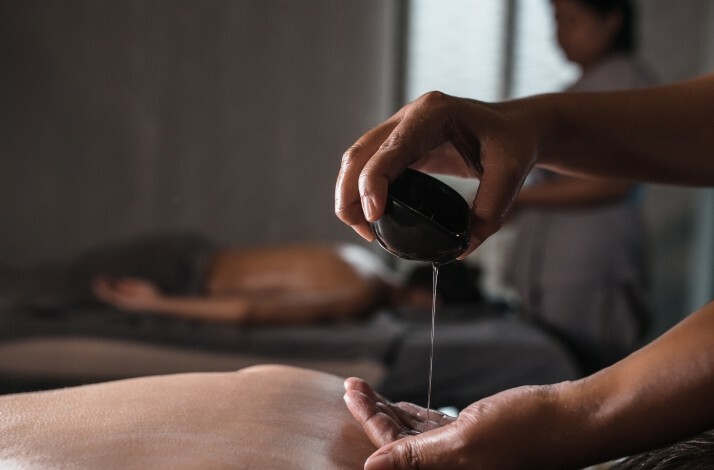 Masseur poring massage oil on hands.