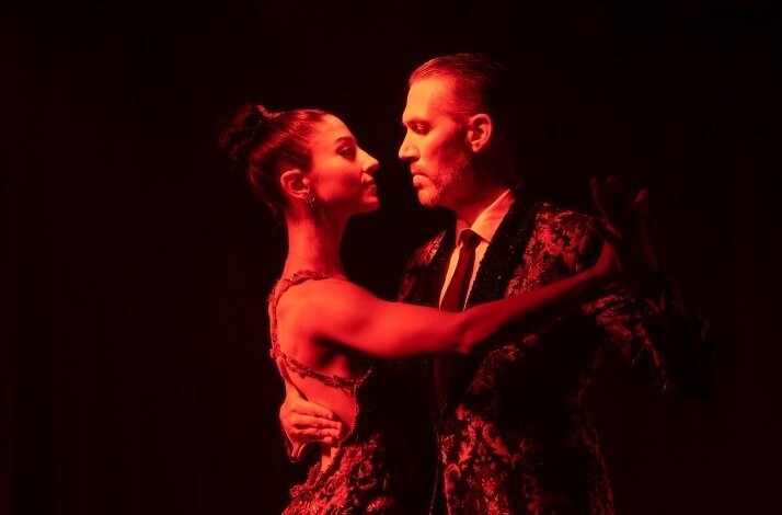 A couple dressed in vintage costumes dance closely under red lights