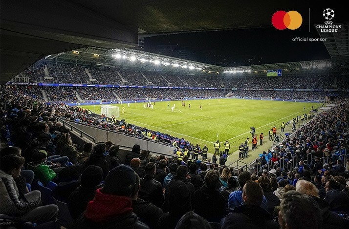 The view on the stadium tribunes filled with  fans during the UEFA Champions League match. The image is featuring Mastercard and UEFA Champions League logos on top right corner