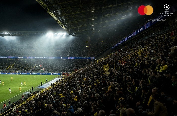 The view on the stadium tribunes filled with  fans during the UEFA Champions League match. The image is featuring Mastercard and UEFA Champions League logos on top right corner