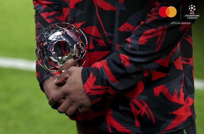 The close shot displaying hands of the football player holding  UEFA Champions League trophy. Image is featuring UEFA and Mastercard logos on top right corner